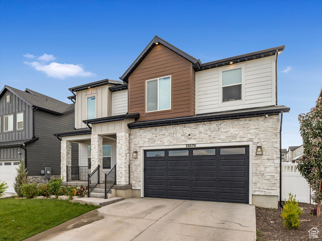 Contemporary house with stone siding, an attached garage, driveway, board and batten siding, and covered porch