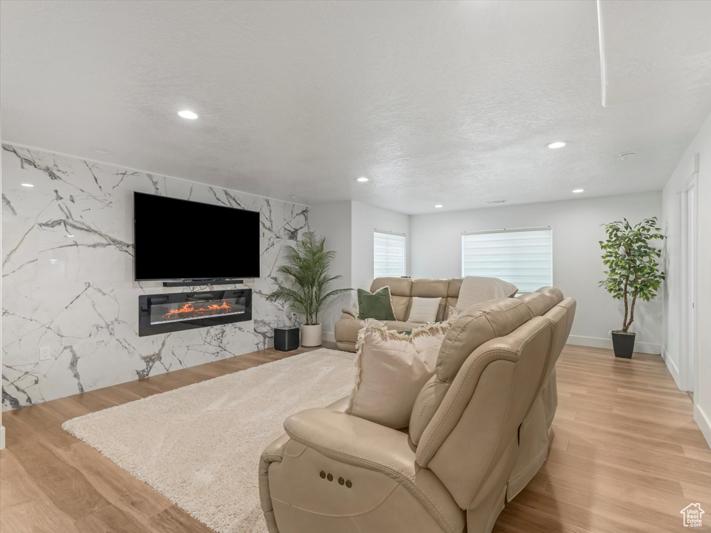 Living area with a high end fireplace, recessed lighting, light wood-style floors, and an accent wall