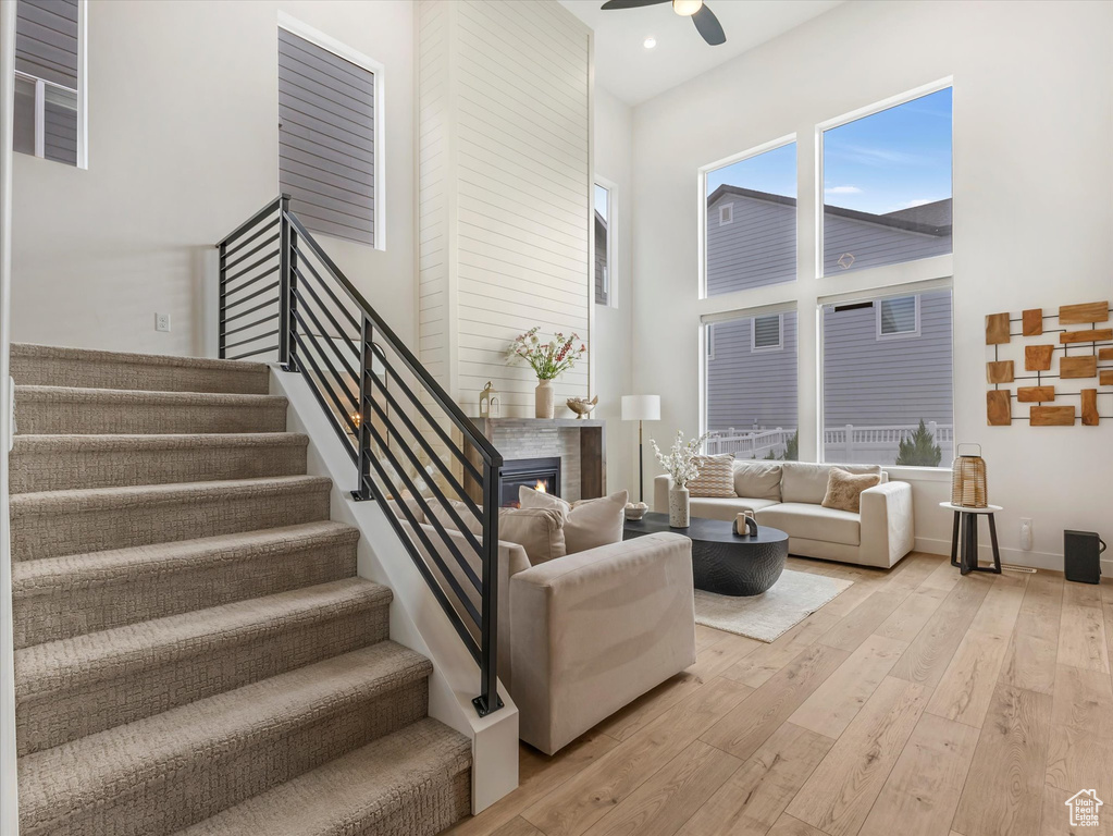 Living area with a towering ceiling, a ceiling fan, light wood-style floors, stairs, and a glass covered fireplace
