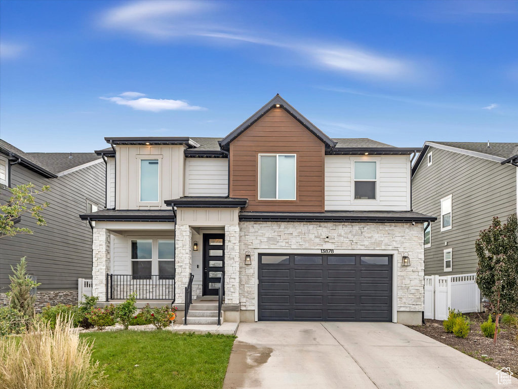 Modern home with concrete driveway, stone siding, a garage, covered porch, and board and batten siding