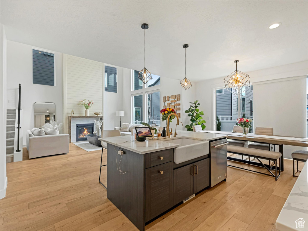 Kitchen featuring stainless steel dishwasher, dark brown cabinetry, a glass covered fireplace, light wood-type flooring, and a kitchen bar