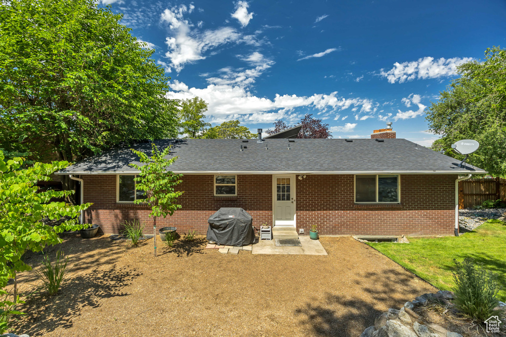 Back of property featuring brick siding, a patio area, roof with shingles, and a chimney