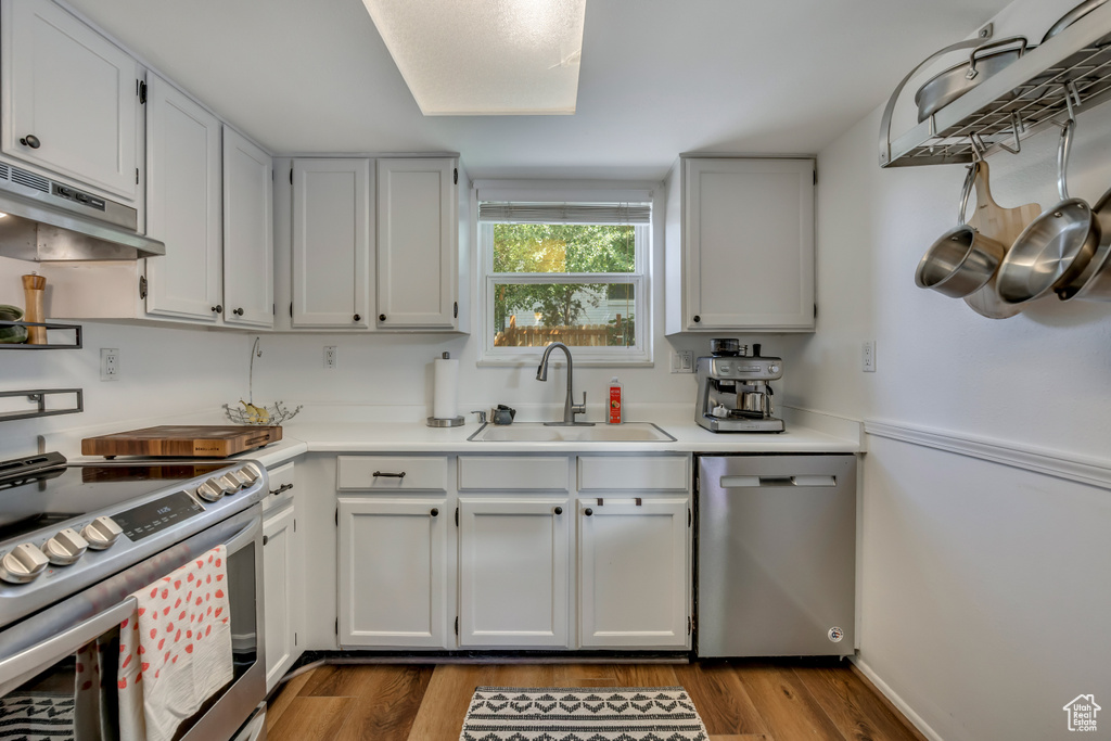 Kitchen with stainless steel appliances, under cabinet range hood, wood finished floors, light countertops, and white cabinets