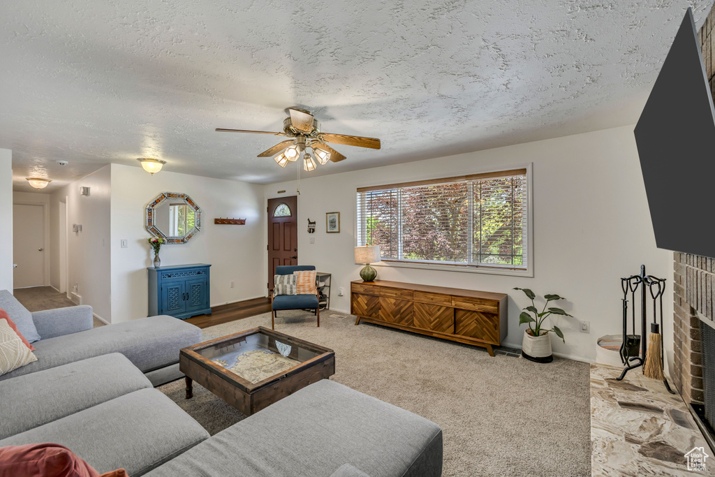 Carpeted living room featuring ceiling fan, a textured ceiling, and a fireplace