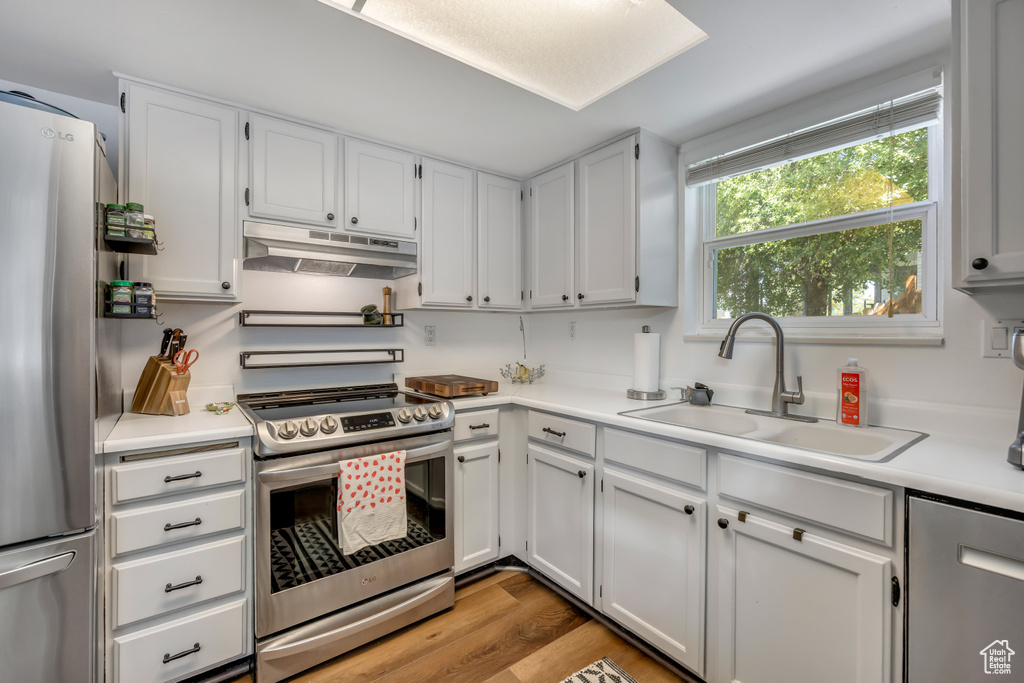Kitchen with appliances with stainless steel finishes, under cabinet range hood, light countertops, white cabinets, and light wood finished floors