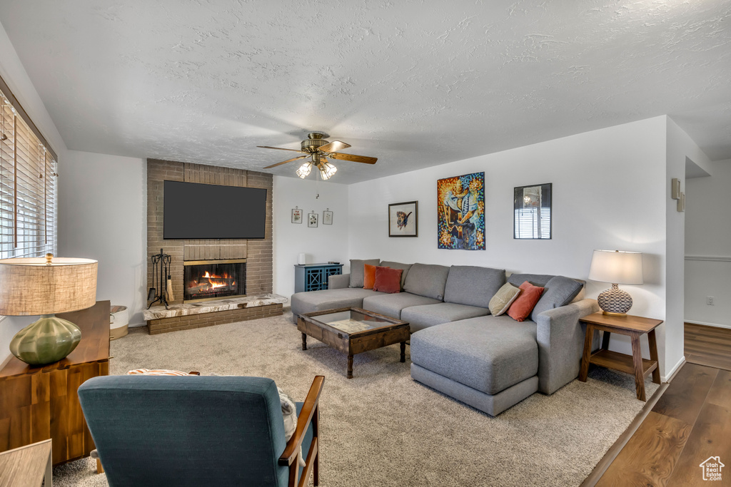 Living room featuring a textured ceiling, ceiling fan, wood finished floors, and a brick fireplace