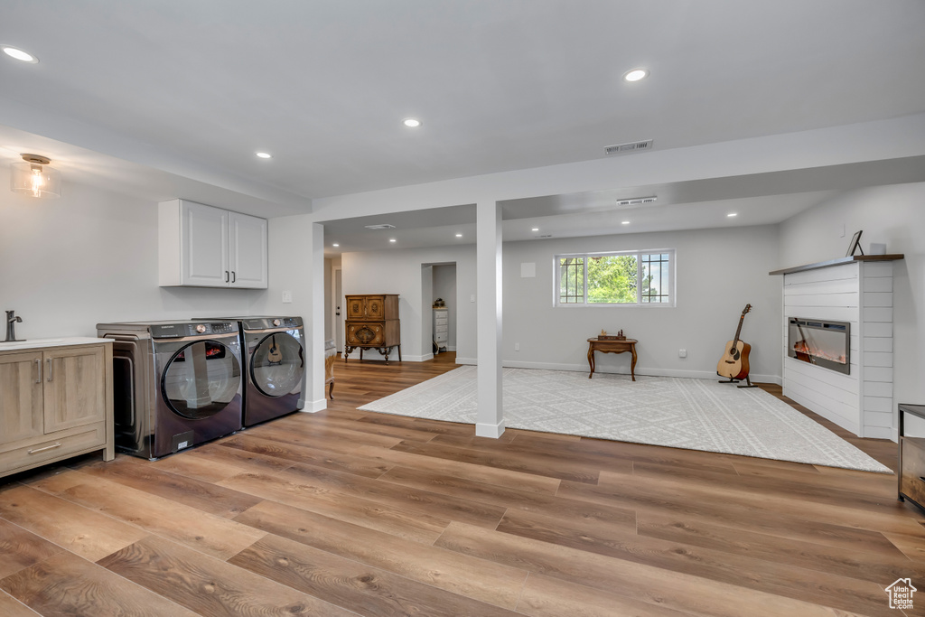 Washroom featuring washing machine and clothes dryer, light wood finished floors, recessed lighting, and a glass covered fireplace