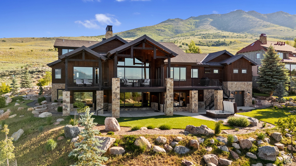 Back of house with stone siding, a patio, a chimney, stairway, and a mountain view