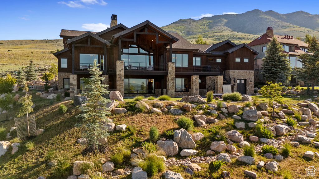 View of front of house featuring stone siding, a balcony, a chimney, and a mountain view