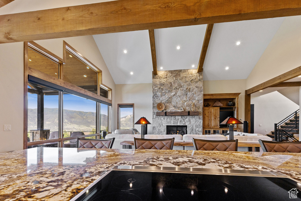 Kitchen with a fireplace, beamed ceiling, open floor plan, light stone countertops, and high vaulted ceiling