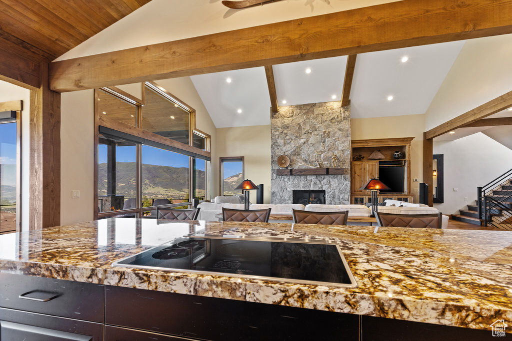 Kitchen with lofted ceiling, black electric cooktop, a stone fireplace, stone counters, and open floor plan