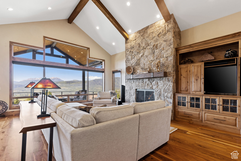 Living room featuring beam ceiling, dark wood-type flooring, a stone fireplace, high vaulted ceiling, and recessed lighting