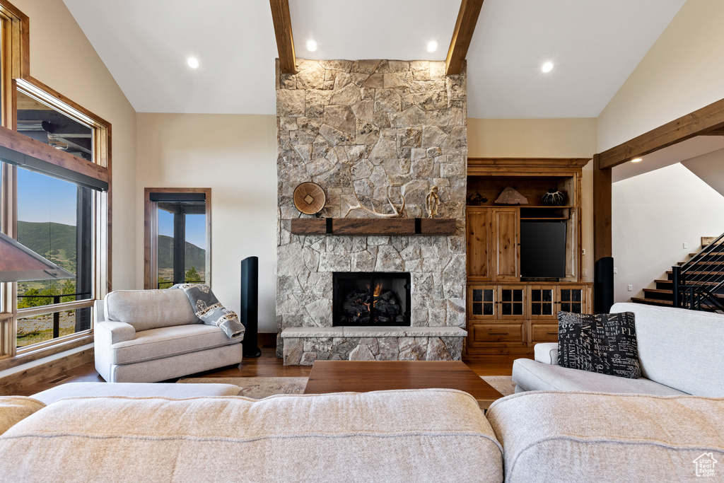 Living area featuring beam ceiling, wood finished floors, a stone fireplace, high vaulted ceiling, and stairway