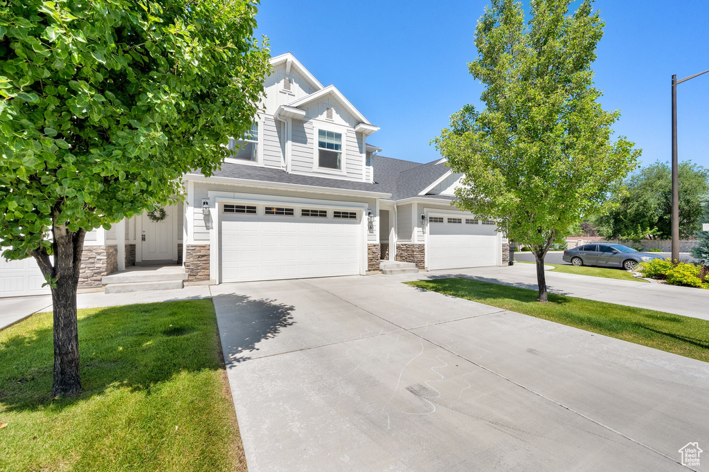 View of front of home with stone siding, driveway, a front lawn, and a garage