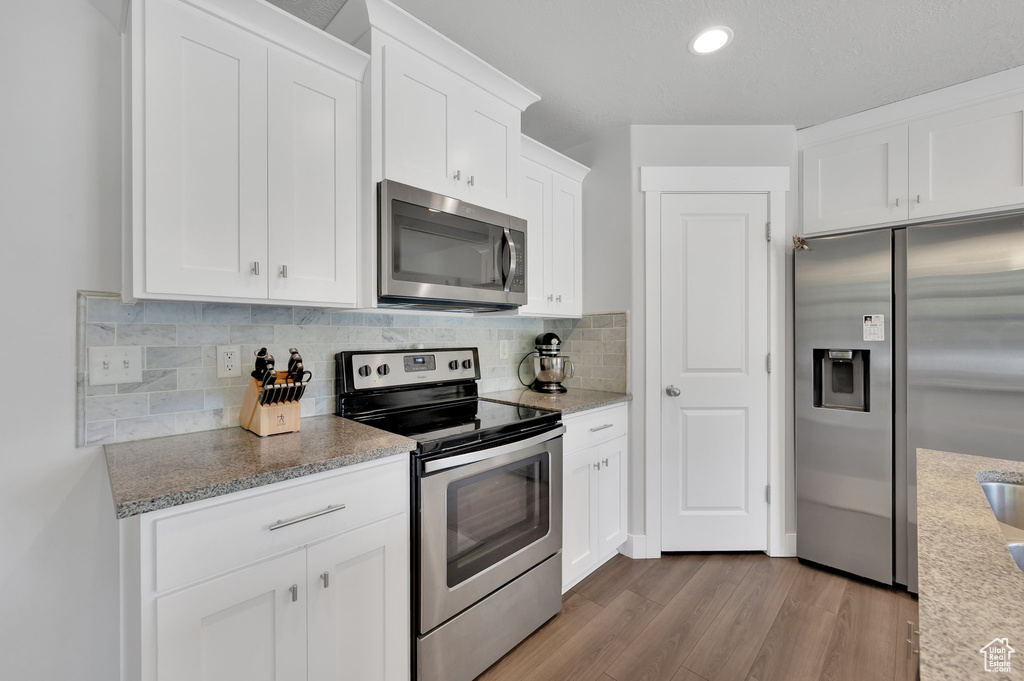 Kitchen featuring appliances with stainless steel finishes, wood finished floors, white cabinets, tasteful backsplash, and recessed lighting