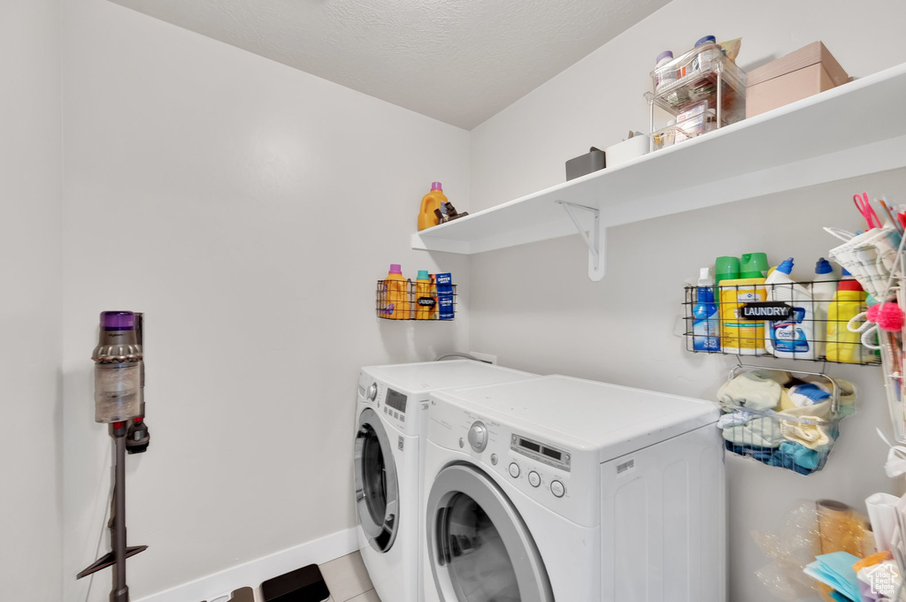Laundry area featuring separate washer and dryer, light tile patterned floors, and a textured ceiling