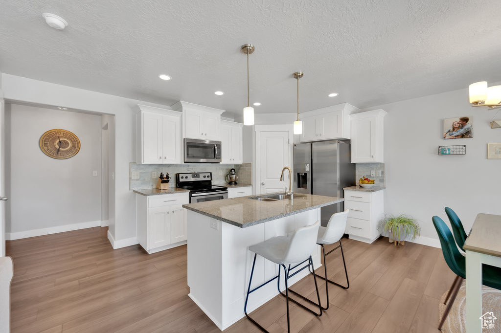 Kitchen with stainless steel appliances, light wood-type flooring, backsplash, a textured ceiling, and recessed lighting