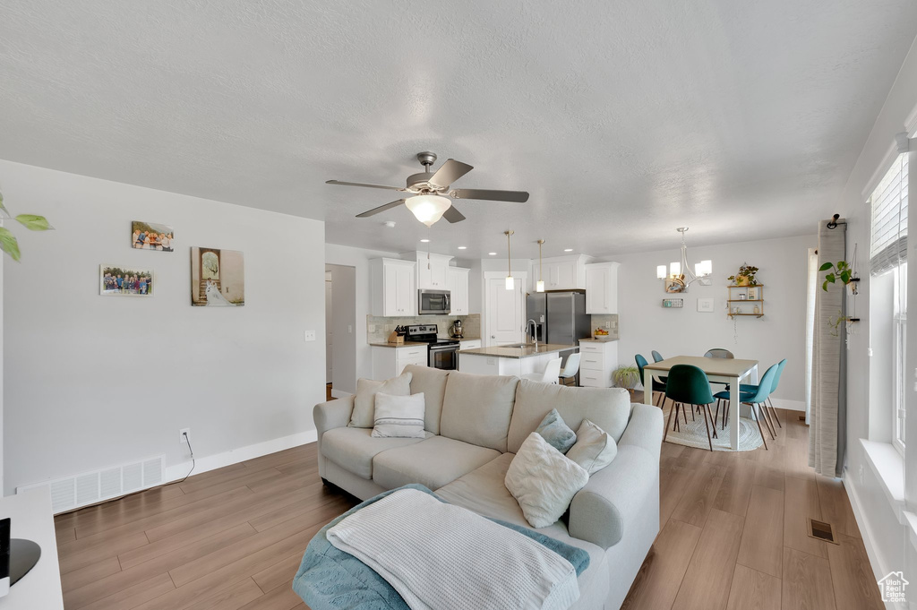 Living area with a chandelier, light wood finished floors, ceiling fan, and recessed lighting