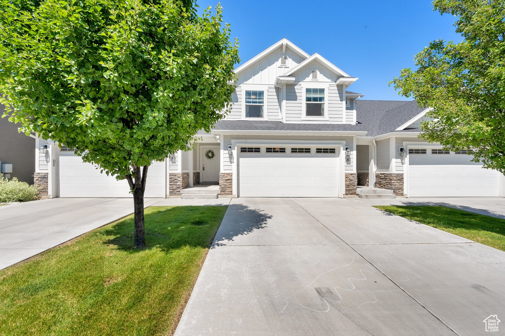 Craftsman inspired home with stone siding, concrete driveway, board and batten siding, and a front lawn