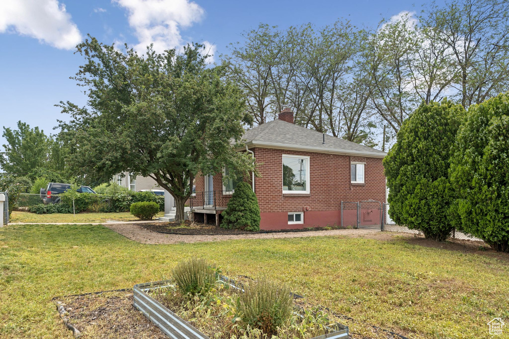 View of side of property with brick siding, a chimney, a vegetable garden, and roof with shingles