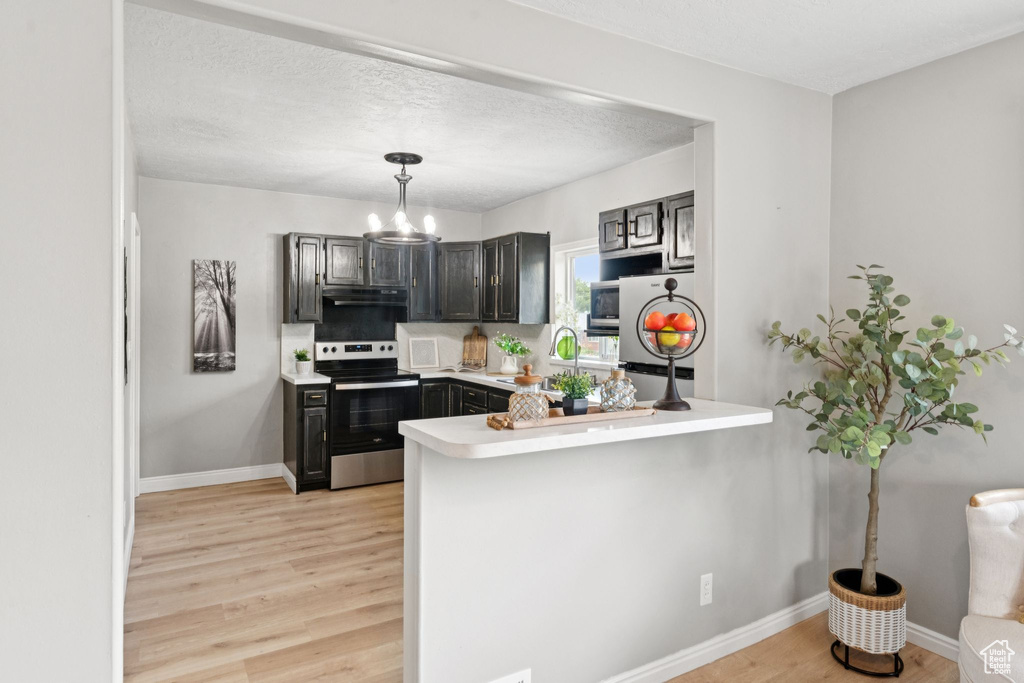 Kitchen with stainless steel appliances, under cabinet range hood, a chandelier, light wood-style floors, and a peninsula
