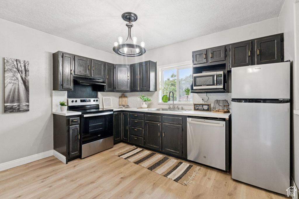 Kitchen with appliances with stainless steel finishes, under cabinet range hood, a chandelier, light countertops, and dark cabinets