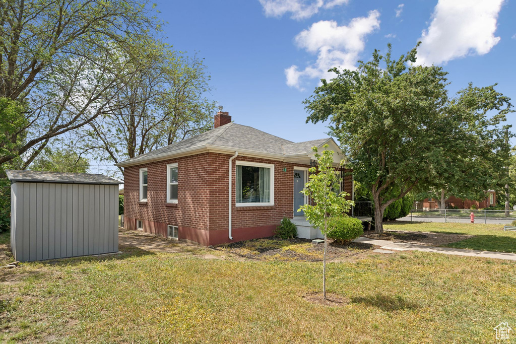 View of side of home featuring brick siding, a chimney, a lawn, and a storage unit