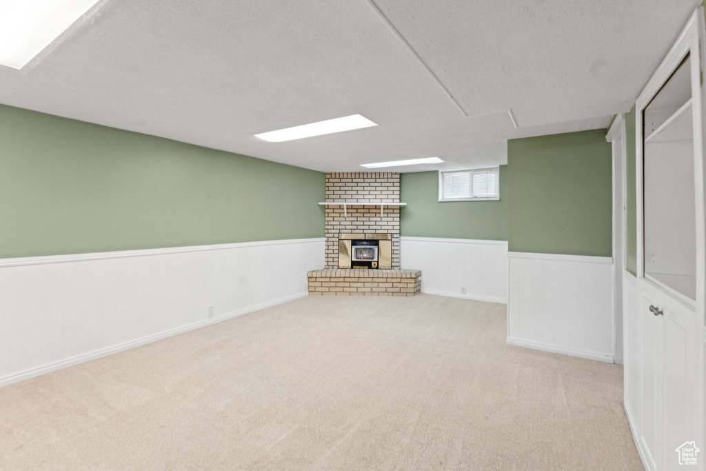 Basement with a wainscoted wall, carpet flooring, a brick fireplace, and a textured ceiling