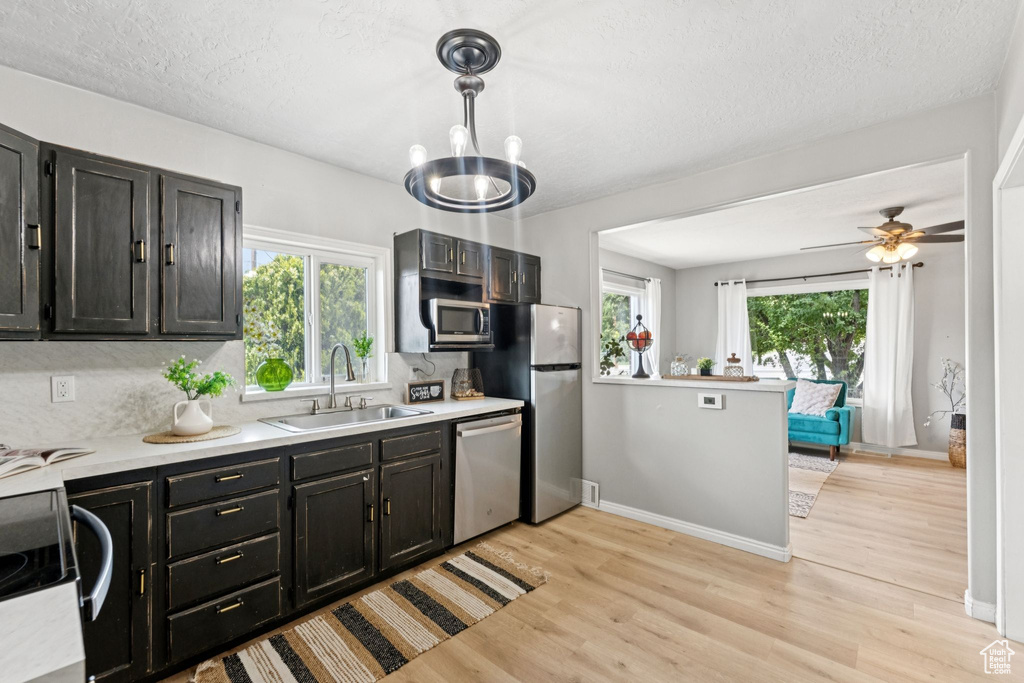 Kitchen with appliances with stainless steel finishes, light countertops, light wood-style floors, pendant lighting, and a textured ceiling
