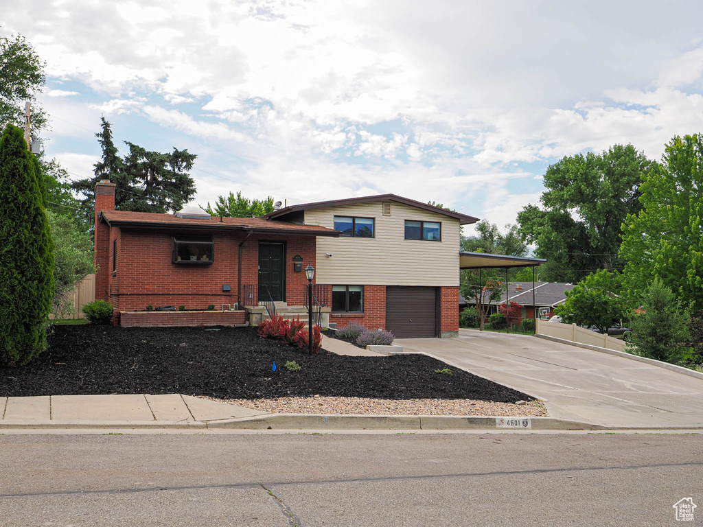 Split level home featuring brick siding, driveway, a garage, and a chimney