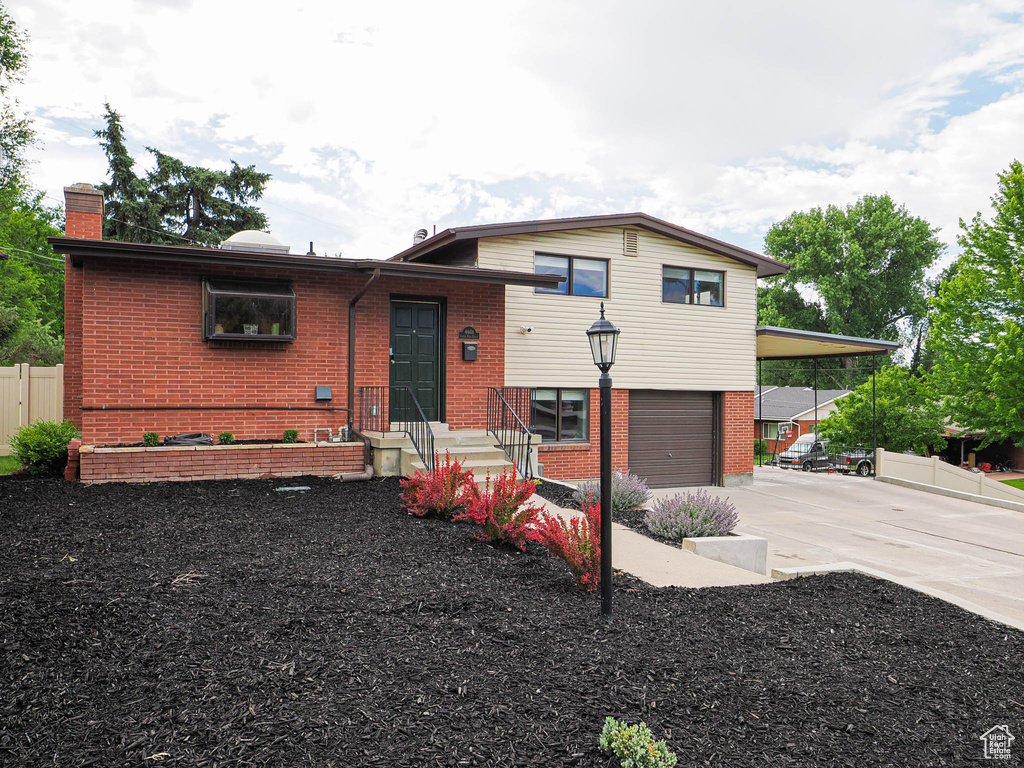 Tri-level home featuring driveway, a garage, a chimney, and brick siding