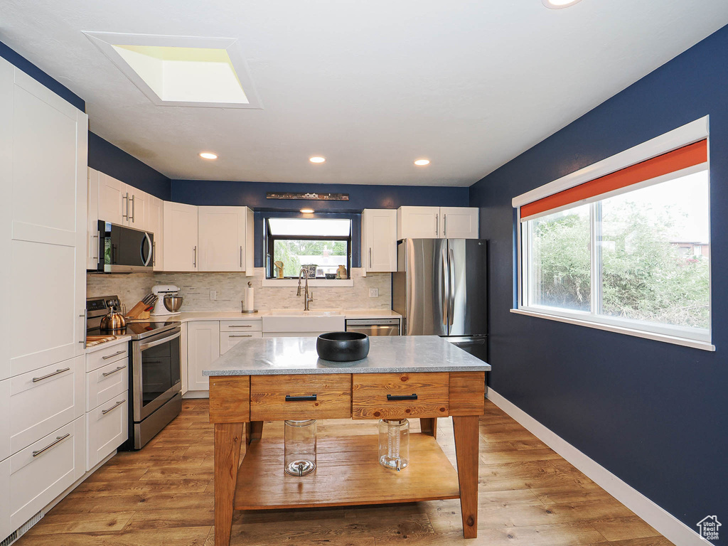 Kitchen with stainless steel appliances, tasteful backsplash, light wood finished floors, white cabinetry, and recessed lighting