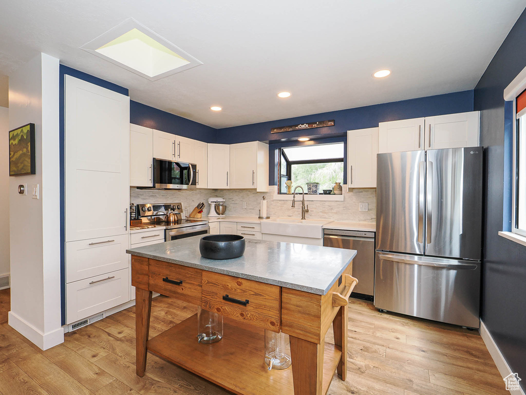 Kitchen featuring stainless steel appliances, white cabinets, decorative backsplash, light wood finished floors, and recessed lighting