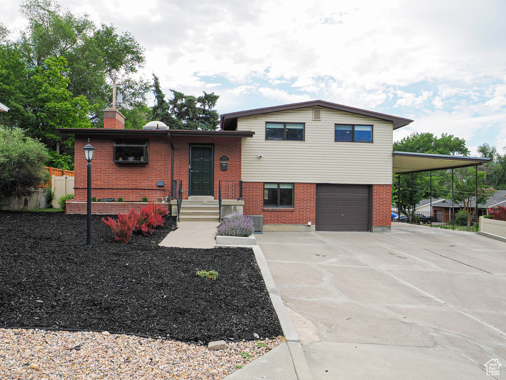 Tri-level home with a garage, brick siding, concrete driveway, and a chimney