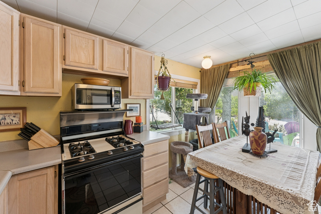 Kitchen with gas range, light brown cabinetry, stainless steel microwave, and light countertops