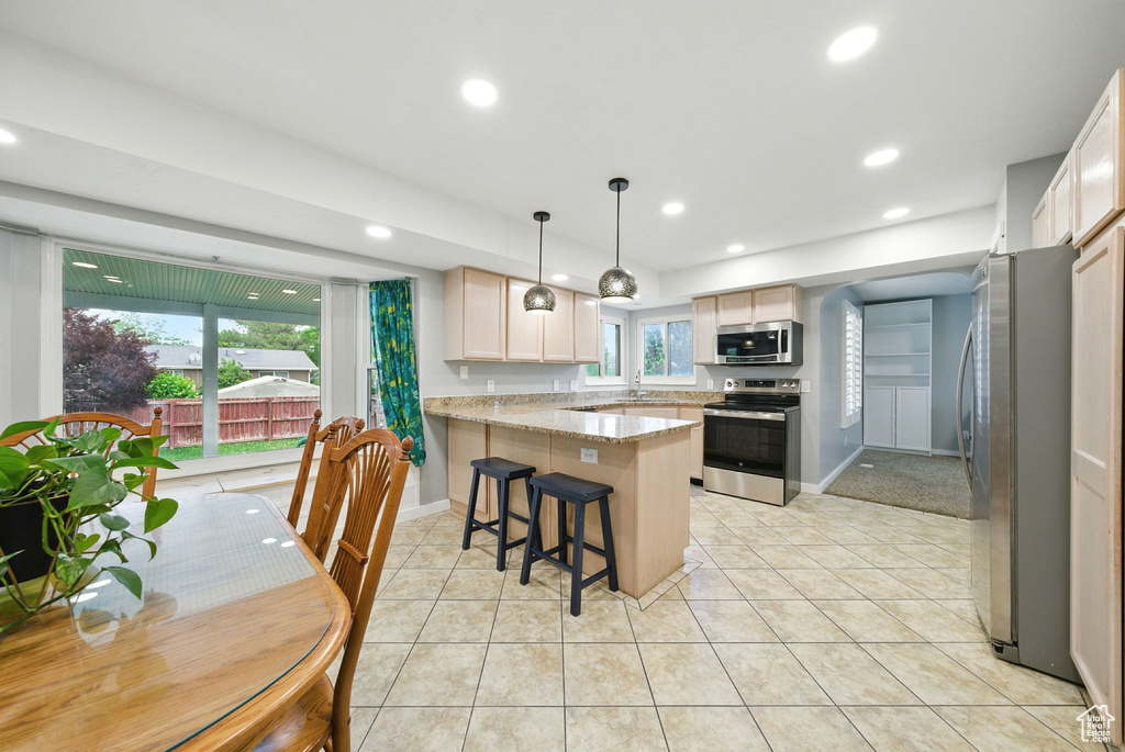 Kitchen featuring appliances with stainless steel finishes, a peninsula, light tile patterned floors, recessed lighting, and a kitchen breakfast bar
