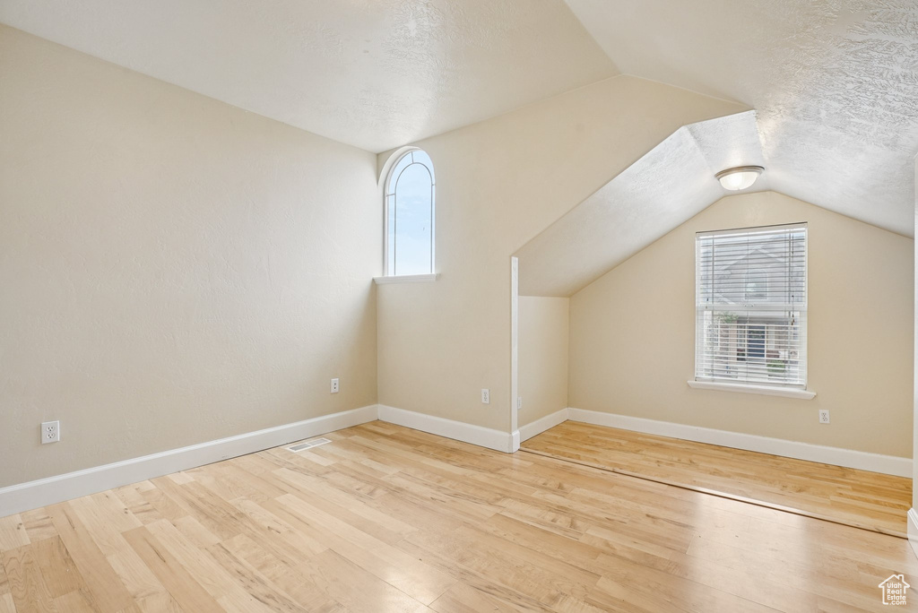 Bonus room with vaulted ceiling, wood finished floors, and a textured ceiling