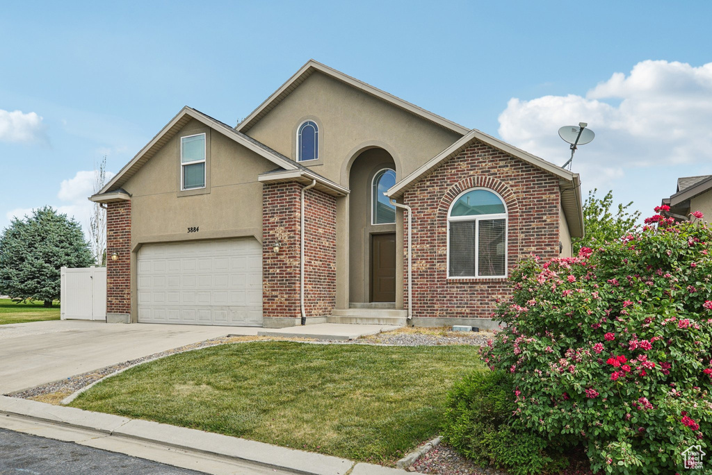 View of front of house with stucco siding, driveway, a front lawn, a garage, and brick siding