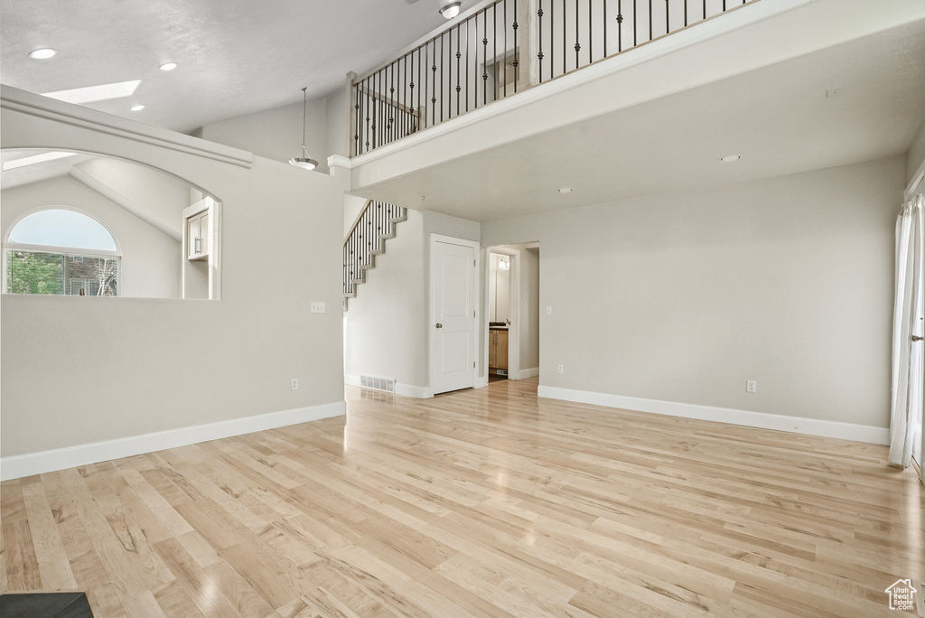 Unfurnished living room with vaulted ceiling, light wood finished floors, recessed lighting, and stairway