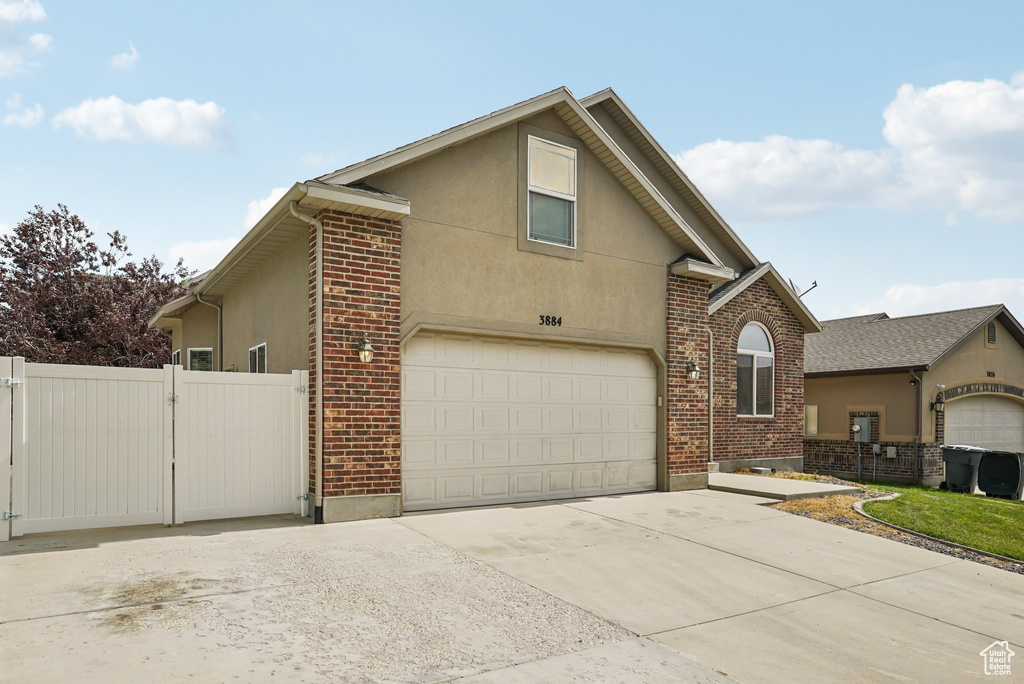 View of front of home with concrete driveway, stucco siding, brick siding, and a gate