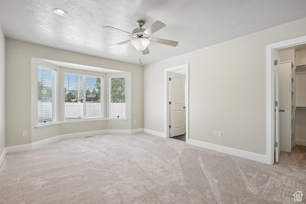 Unfurnished bedroom with a spacious closet, carpet flooring, a textured ceiling, a closet, and a ceiling fan