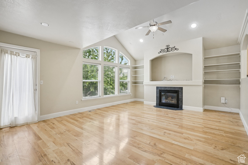 Unfurnished living room with wood finished floors, a fireplace, ceiling fan, vaulted ceiling, and built in features