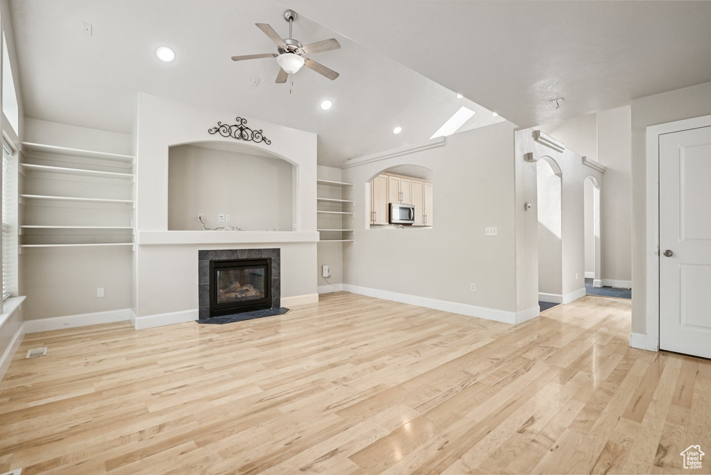 Unfurnished living room featuring lofted ceiling, a tile fireplace, a ceiling fan, light wood-style flooring, and arched walkways