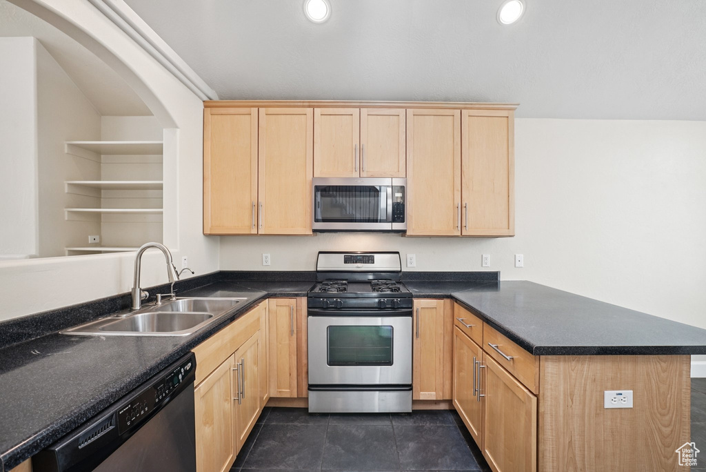 Kitchen with appliances with stainless steel finishes, a peninsula, light brown cabinets, dark countertops, and recessed lighting