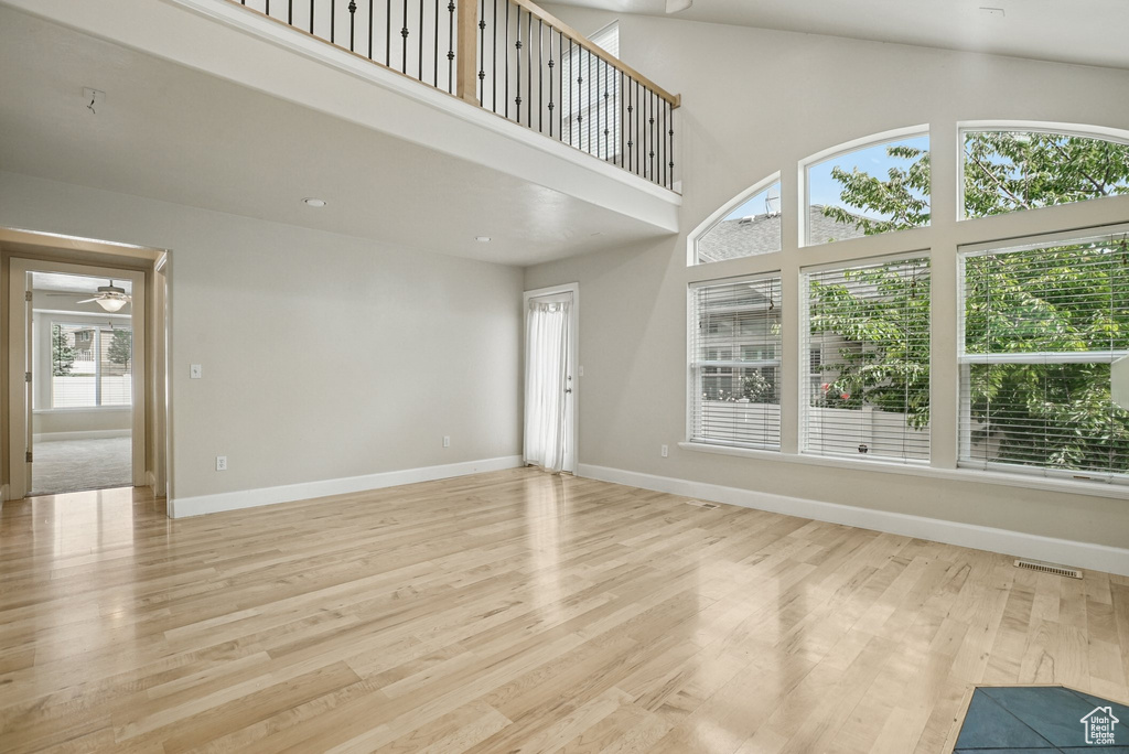 Unfurnished living room featuring light wood-type flooring, a ceiling fan, and a towering ceiling