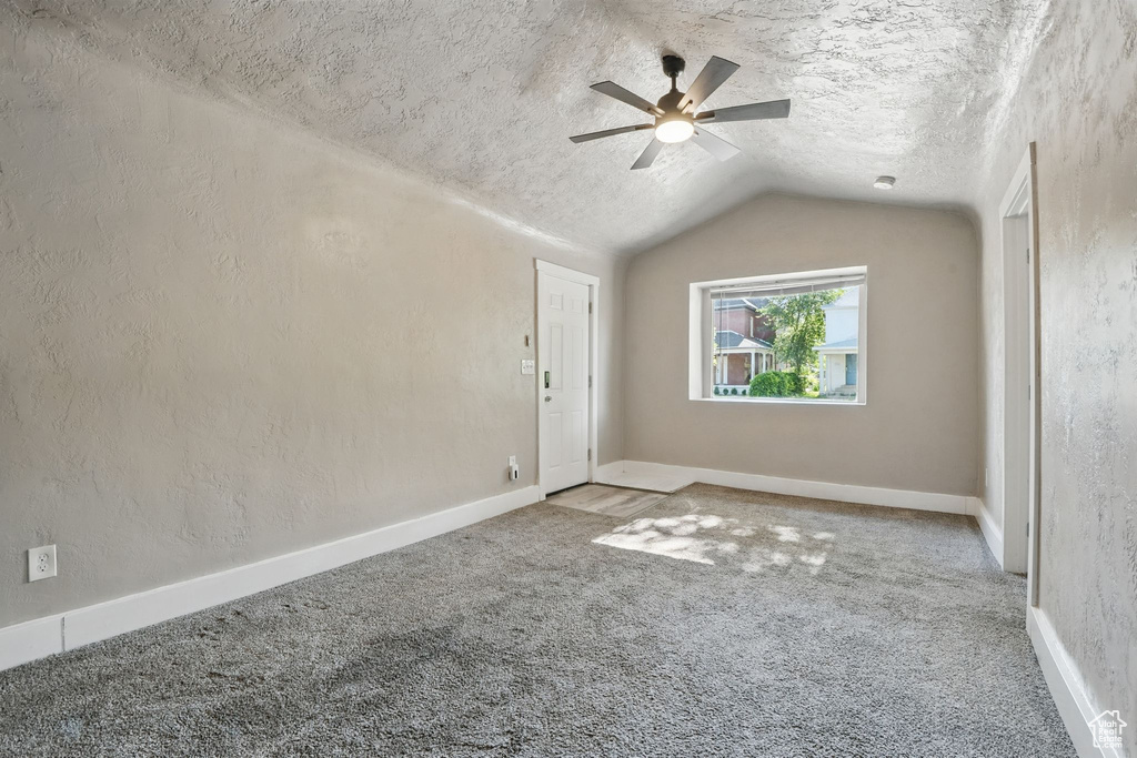 Unfurnished room featuring a textured ceiling, carpet, ceiling fan, and lofted ceiling