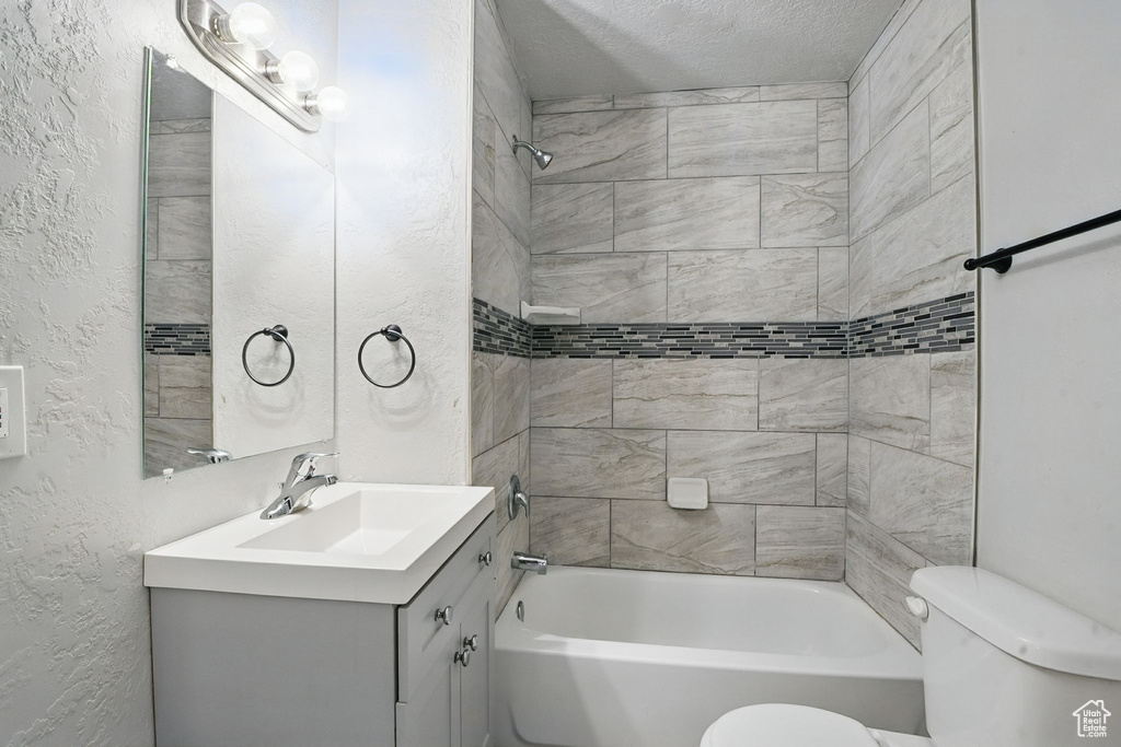 Full bathroom with a textured wall, vanity, shower / bath combination, and a textured ceiling