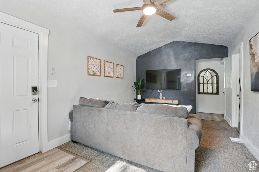 Living area featuring vaulted ceiling, ceiling fan, and a textured ceiling