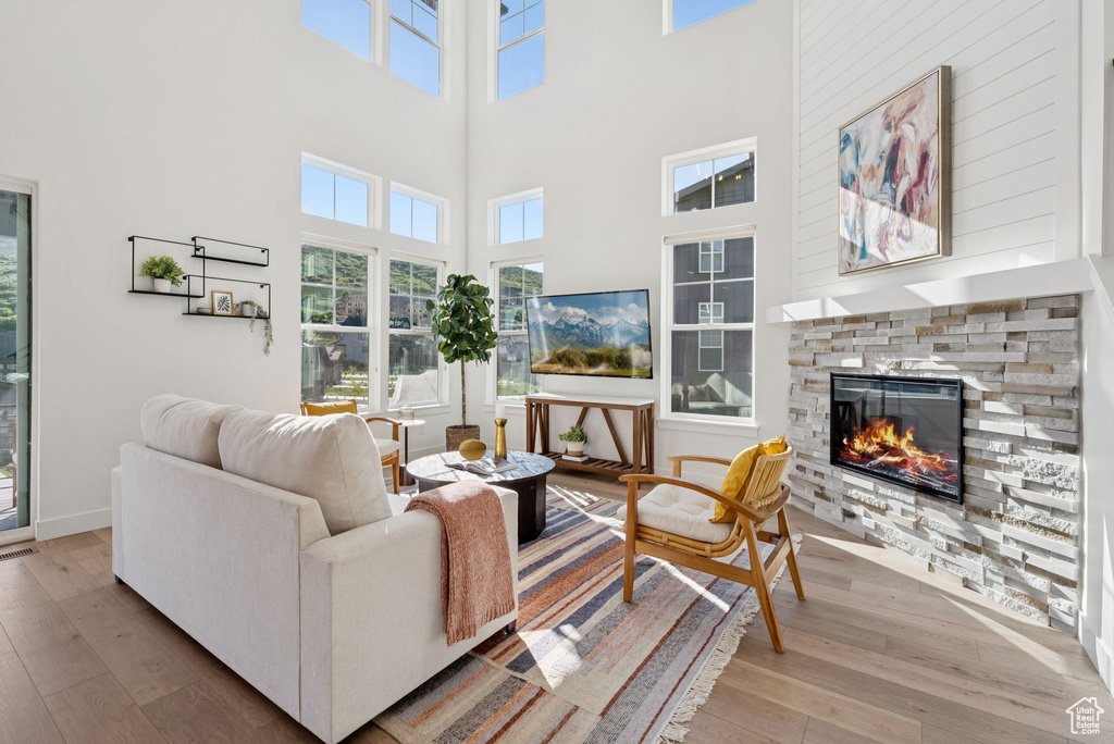 Living area with wood finished floors, a stone fireplace, healthy amount of natural light, and a towering ceiling