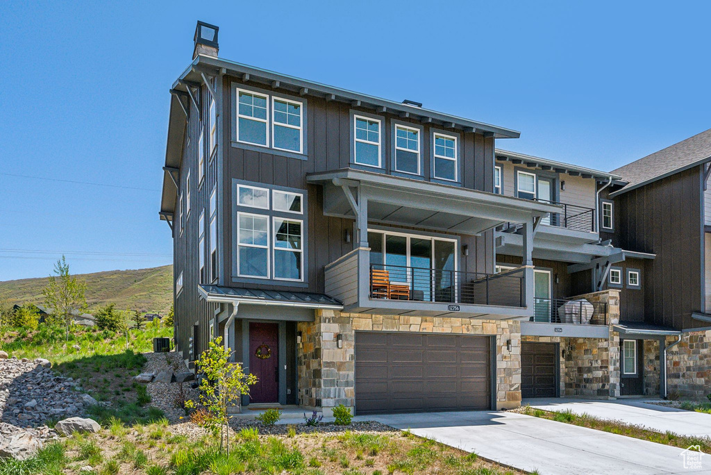 View of front of house with board and batten siding, an attached garage, stone siding, and concrete driveway